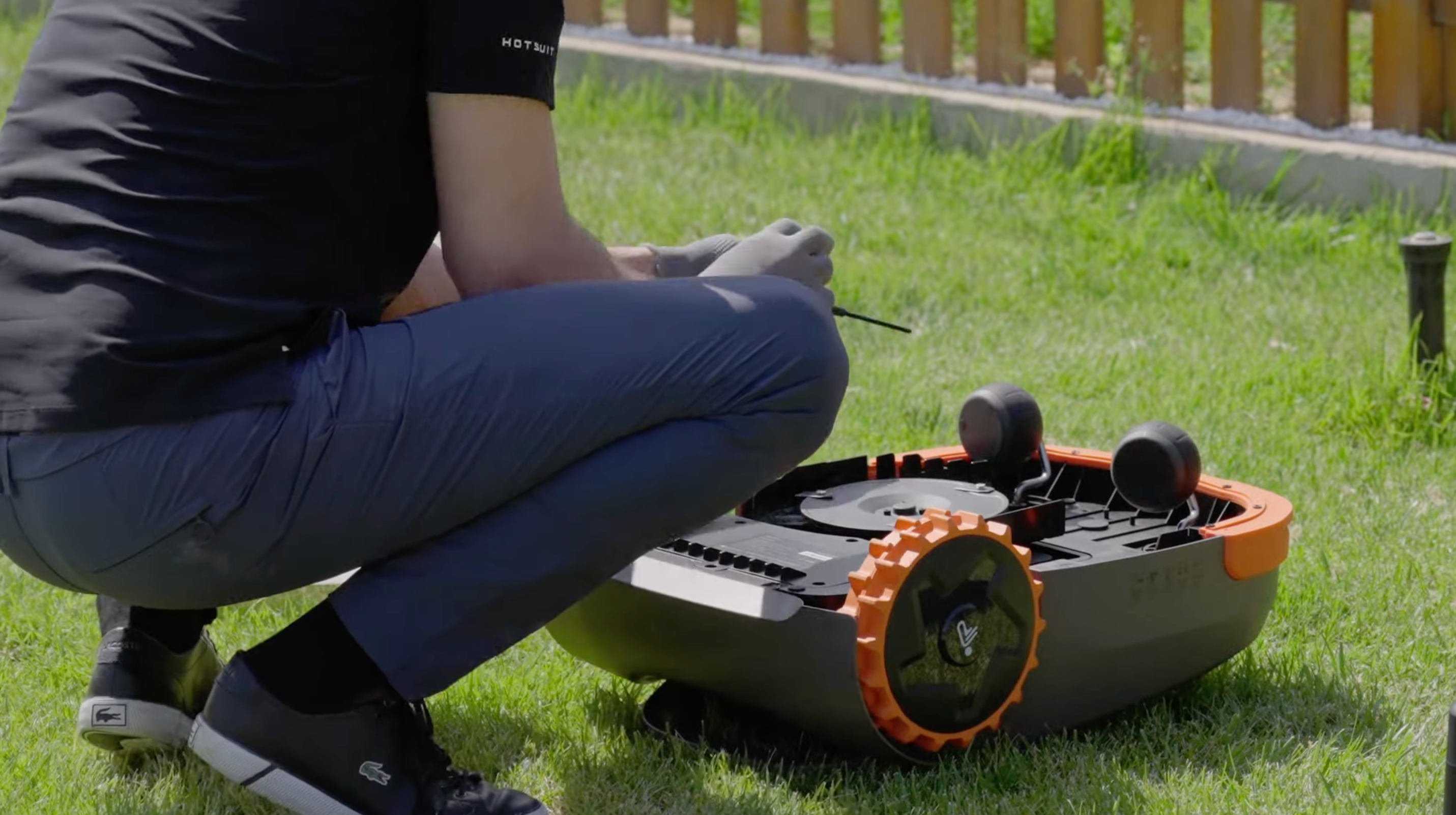 Geheel overzicht van een gebruiker die de maaischijf van een omgedraaide grasrobot inspecteert voor het vervangen van de mesjes.
